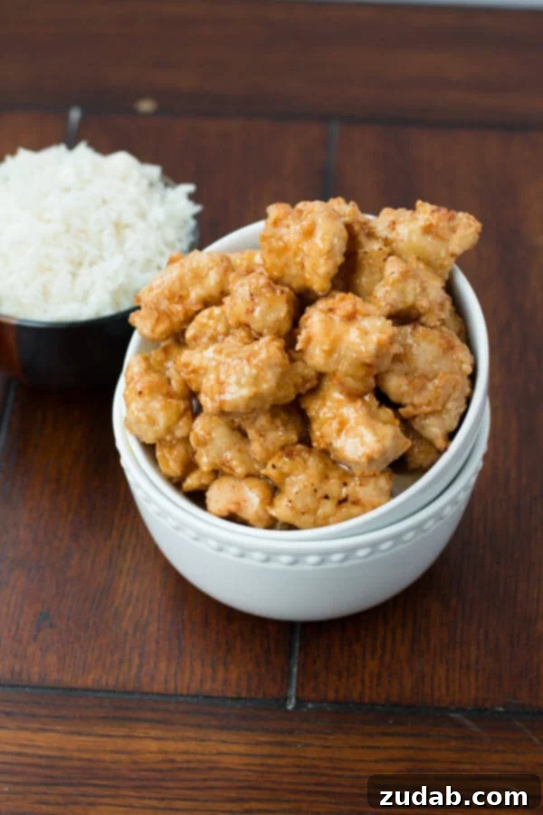 This asian crispy honey chicken was so good and turned out perfect! ohsweetbasil.com Asian Crispy Honey Chicken in two white bowls next to a black bowl of white rice on a wooden table.