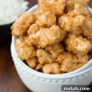 Crispy Honey Chicken in a white bowl next to a small bowl of white rice on a wooden table.