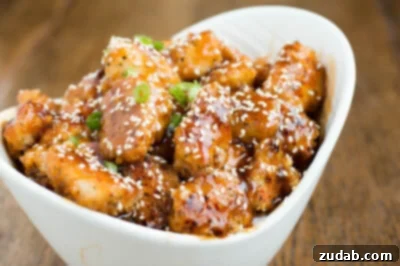 Sticky Honey Garlic Crispy Chicken 3 Baked Sesame Chicken in a white serving bowl on a wooden table.