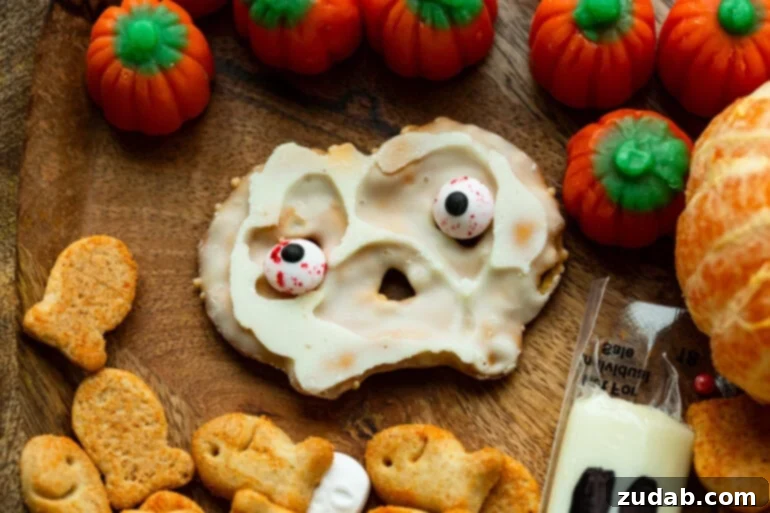 Spooky Simple Snack Platter 3 A white chocolate-covered pretzel crisp adorned with edible googly eyes, placed prominently on a Halloween-themed snack board to showcase a simple yet effective spooky treat decoration.