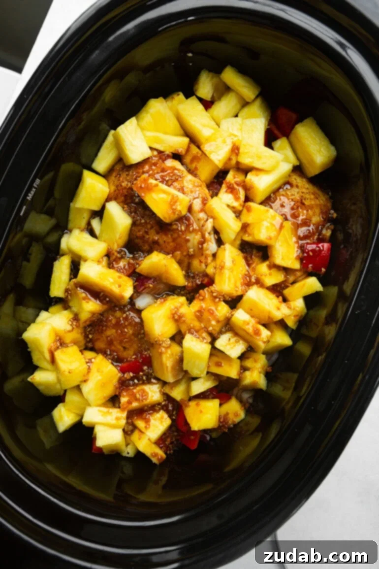 Sweet and Tangy Slow Cooker Pineapple Chicken 4 Golden chicken thighs nestled in a rich cooking sauce, topped with bright chunks of pineapple, red bell pepper, and purple onion, ready for slow cooking