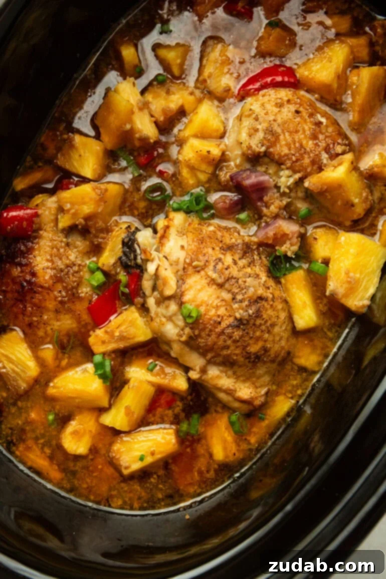 Sweet and Tangy Slow Cooker Pineapple Chicken 6 A black crockpot filled with cooked pineapple teriyaki chicken thighs, tender pineapple chunks, red bell peppers, purple onions, and a sprinkle of chopped green onions