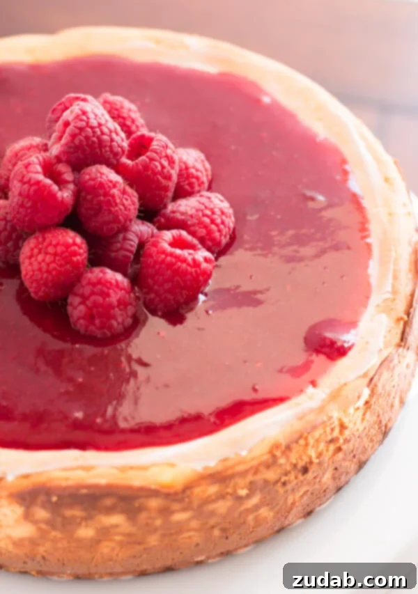 A close-up view of a slice of Greek Yogurt New York Cheesecake, showcasing its rich, creamy texture and the vibrant berry sauce drizzled on top.