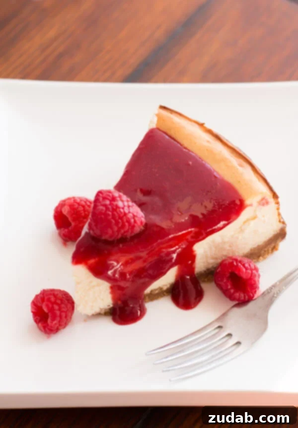 A beautifully plated slice of Greek Yogurt New York Cheesecake with a generous drizzle of homemade brown sugar berry sauce.