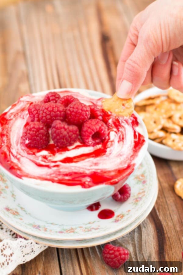 Sharing the Joy: Raspberry Cheesecake Dip at Gatherings A group of friends enjoying the no-bake raspberry cheesecake dip at a social event, dipping mini pretzel crisps into the creamy, fruity dessert. Highlights the social aspect and portability of the dip.