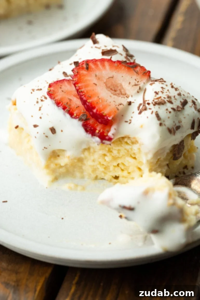 Mexican Tres Leches Cake Recipe 3 a photo of a moist piece of tres leches cake topped with sliced strawberries and shaved chocolate with a bite removed by a fork