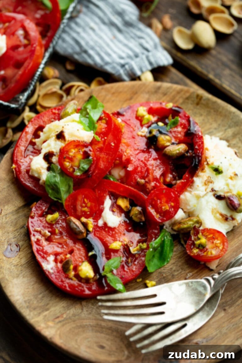 A single serving of Caprese salad, artfully arranged on a small wooden plate, showcasing sliced tomatoes, fresh mozzarella, vibrant basil, and toasted pistachios, with a delicate drizzle of balsamic glaze.