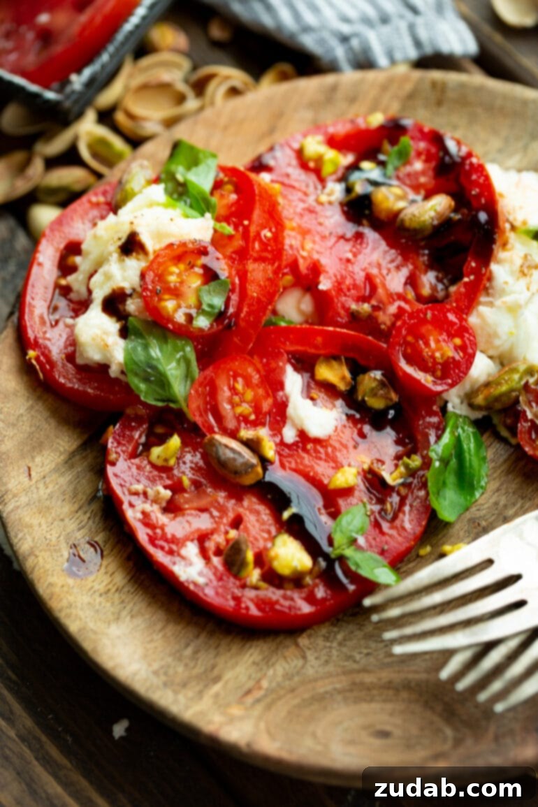 A single serving of Caprese salad with pistachios, presented on a small wooden salad plate, featuring colorful tomato slices, fresh mozzarella, green basil, and toasted pistachios, ready for a light and elegant meal.
