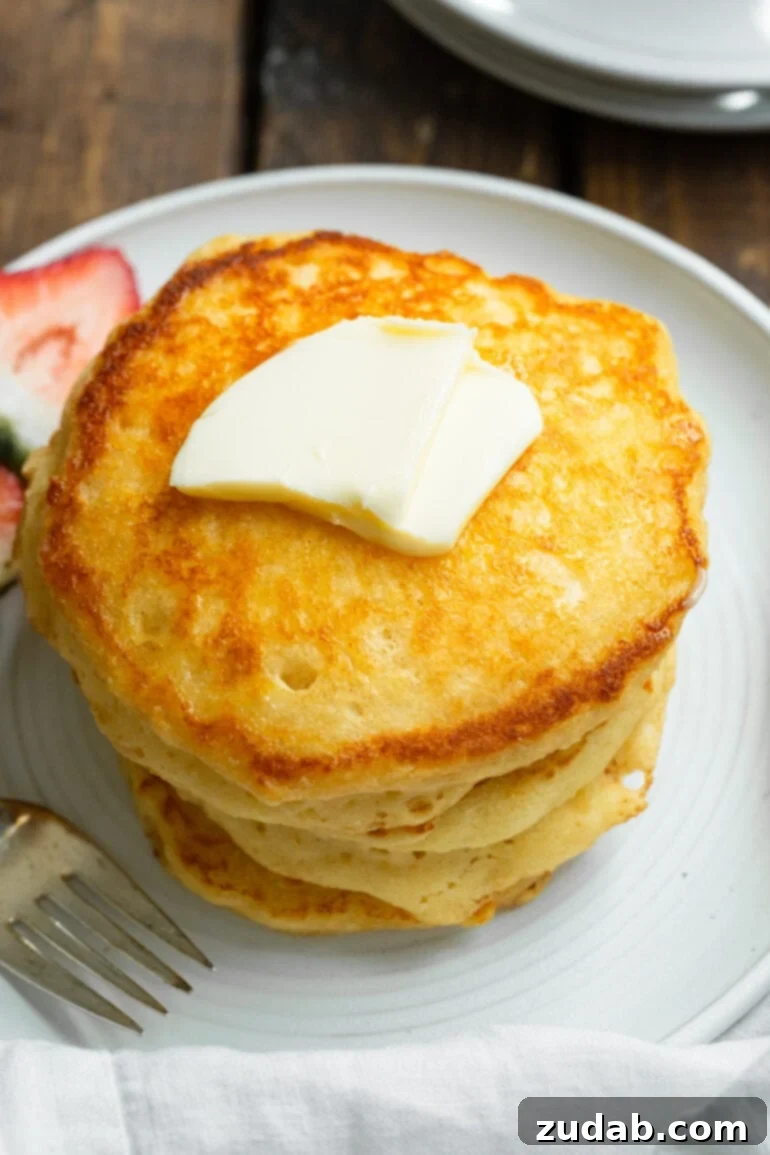 Melt-Away Buttermilk Pancakes 3 A stunning photo of a tall, opulent stack of golden, fluffy buttermilk pancakes, elegantly topped with a generous pat of melting butter. This image perfectly encapsulates the rich, indulgent quality of our melt-in-your-mouth buttermilk pancakes, promising a truly delightful and satisfying breakfast that champions flavor and texture.