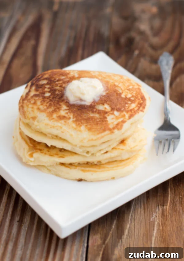The absolute best recipe (after testing hundreds) for buttermilk pancakes. In fact, these are melt in your mouth buttermilk pancakes! A beautifully arranged stack of perfectly fluffy buttermilk pancakes resting on a crisp white plate, prepared to be adorned with your favorite toppings. This image elegantly captures the simple, comforting essence of a classic homemade buttermilk pancake breakfast, making it perfect for any morning, be it a busy weekday or a leisurely weekend.
