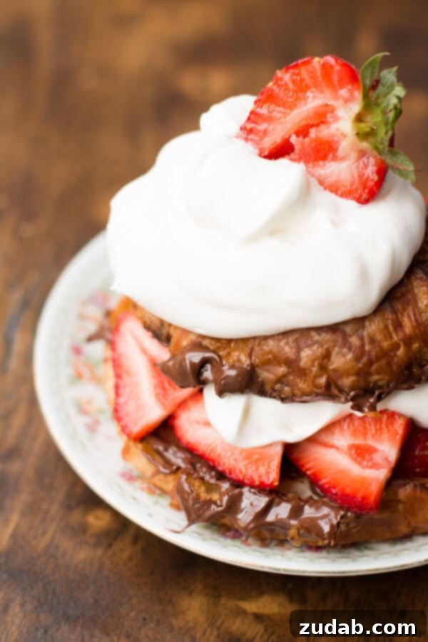 Decadent Grilled Nutella Strawberry Croissant with Berries and Whipped Cream A close-up shot of a perfectly grilled croissant filled with Nutella, sliced fresh strawberries, and topped with a generous swirl of whipped cream.