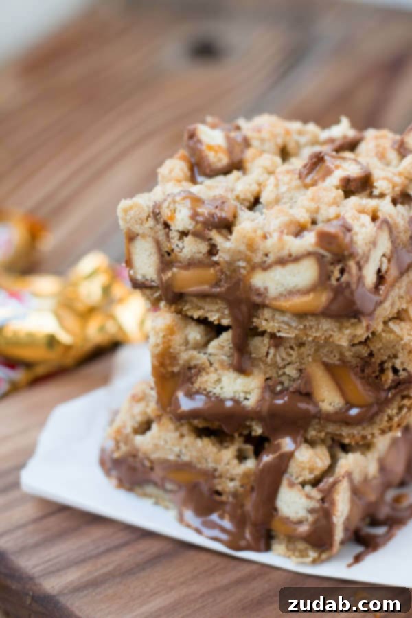 Ultimate Twix Caramelitas Dessert Bars Delicious Twix Caramelitas stacked high, showing layers of oatmeal crust, chocolate, and caramel with Twix candy pieces.