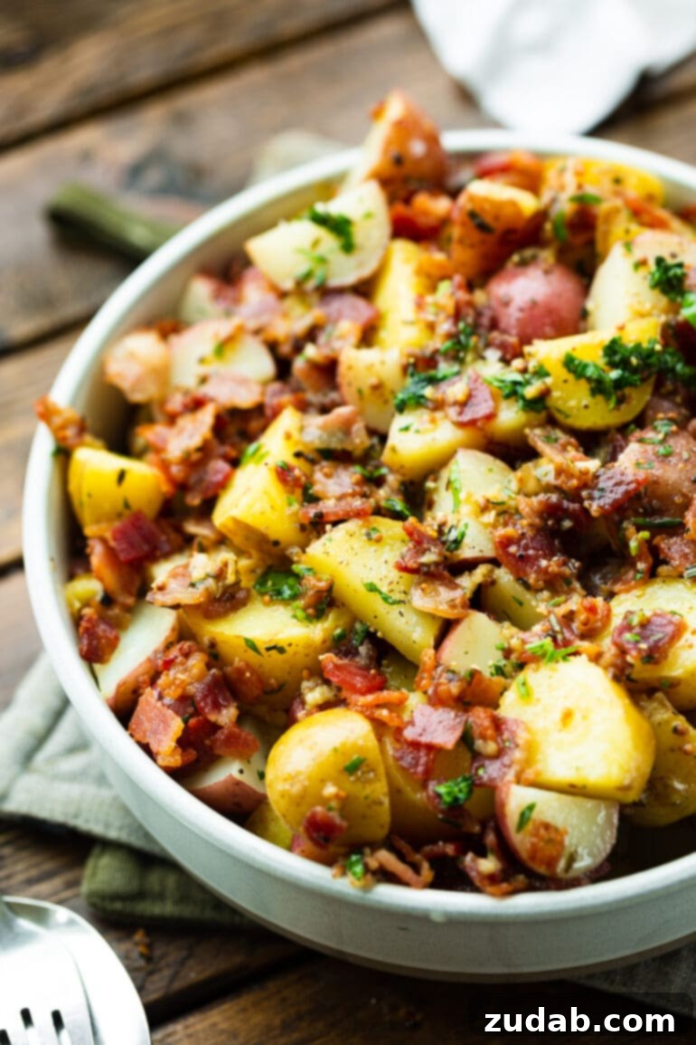 A photo of a bowl of warm German potato salad, glistening with its tangy dressing, adorned with golden potatoes, crisp bacon bits, and vibrant fresh parsley.