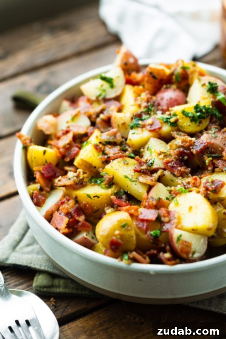 A vibrant photo of warm German potato salad, abundantly filled with cooked potatoes, crispy bacon crumbles, minced garlic, and chopped fresh parsley.
