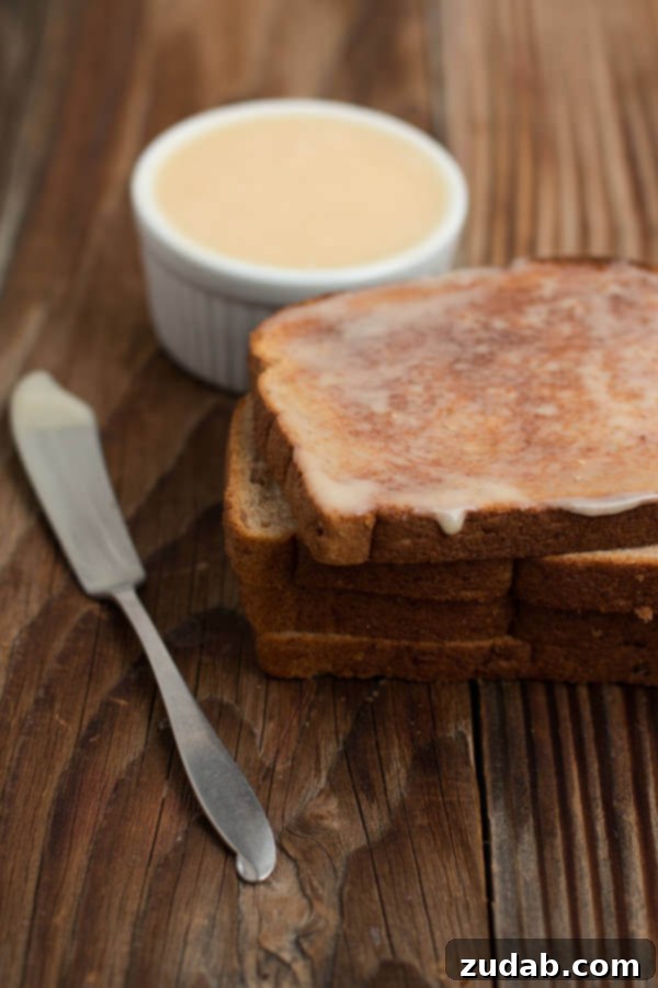 The best blasted honey butter ever. ohsweetbasil.com A beautiful shot of honey butter melting onto a warm piece of bread, showcasing its smooth consistency and delicious appeal.