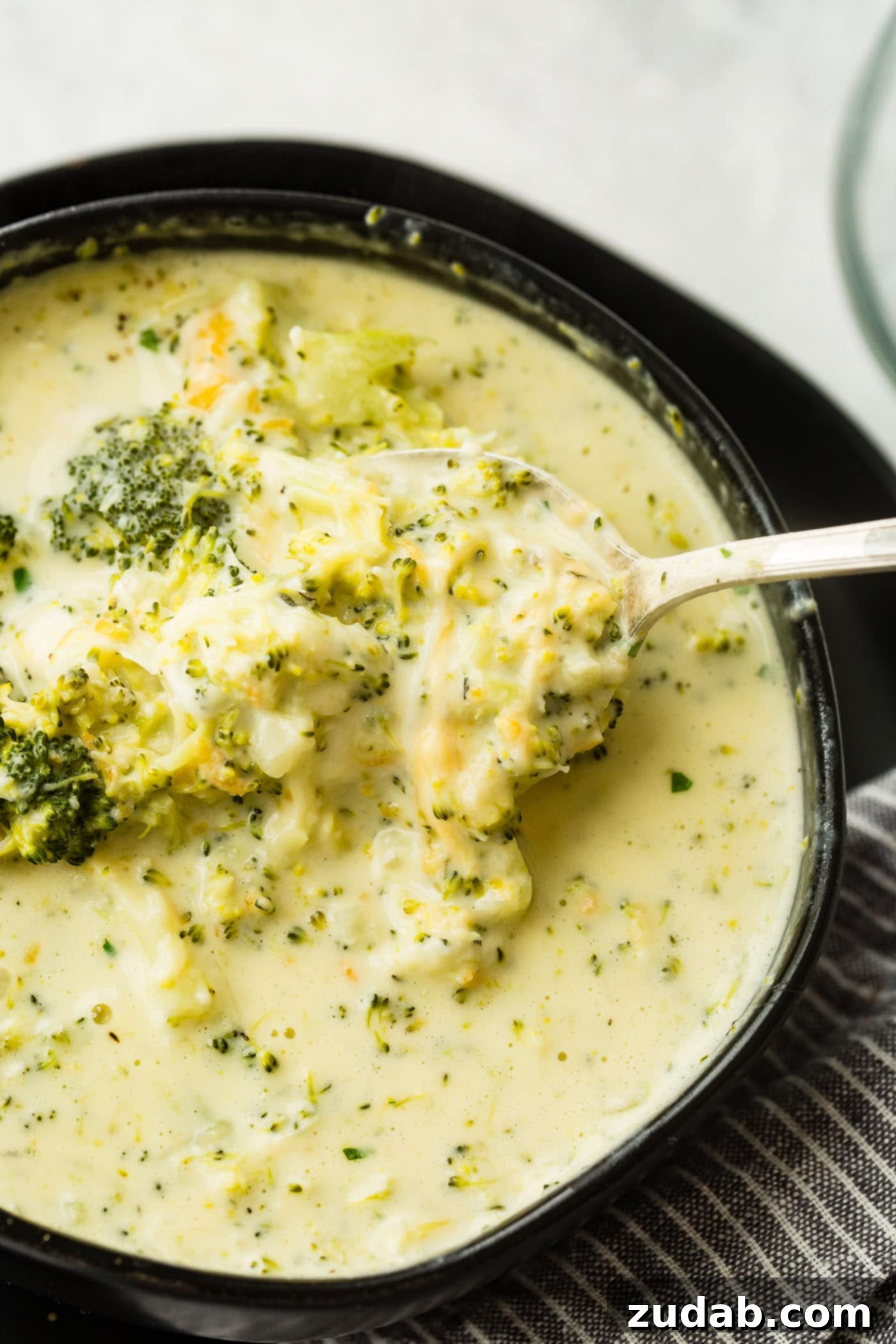 Cozy Slow Cooker Broccoli Cheddar Bliss 5 A black bowl full of slow cooker broccoli cheese soup with extra cheese on top, ready for a cozy meal.