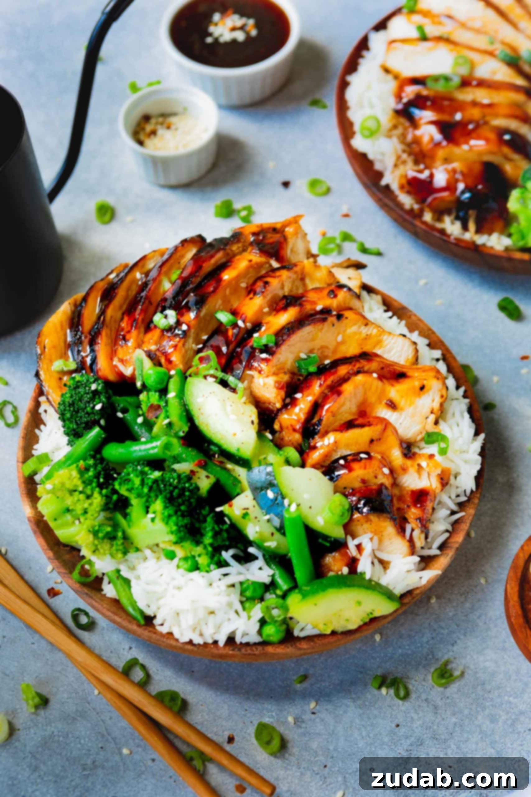 A plate of fluffy white rice topped with generous portions of glistening teriyaki chicken, accompanied by vibrant steamed broccoli, green beans, and zucchini. The sauce beautifully coats each piece of chicken.