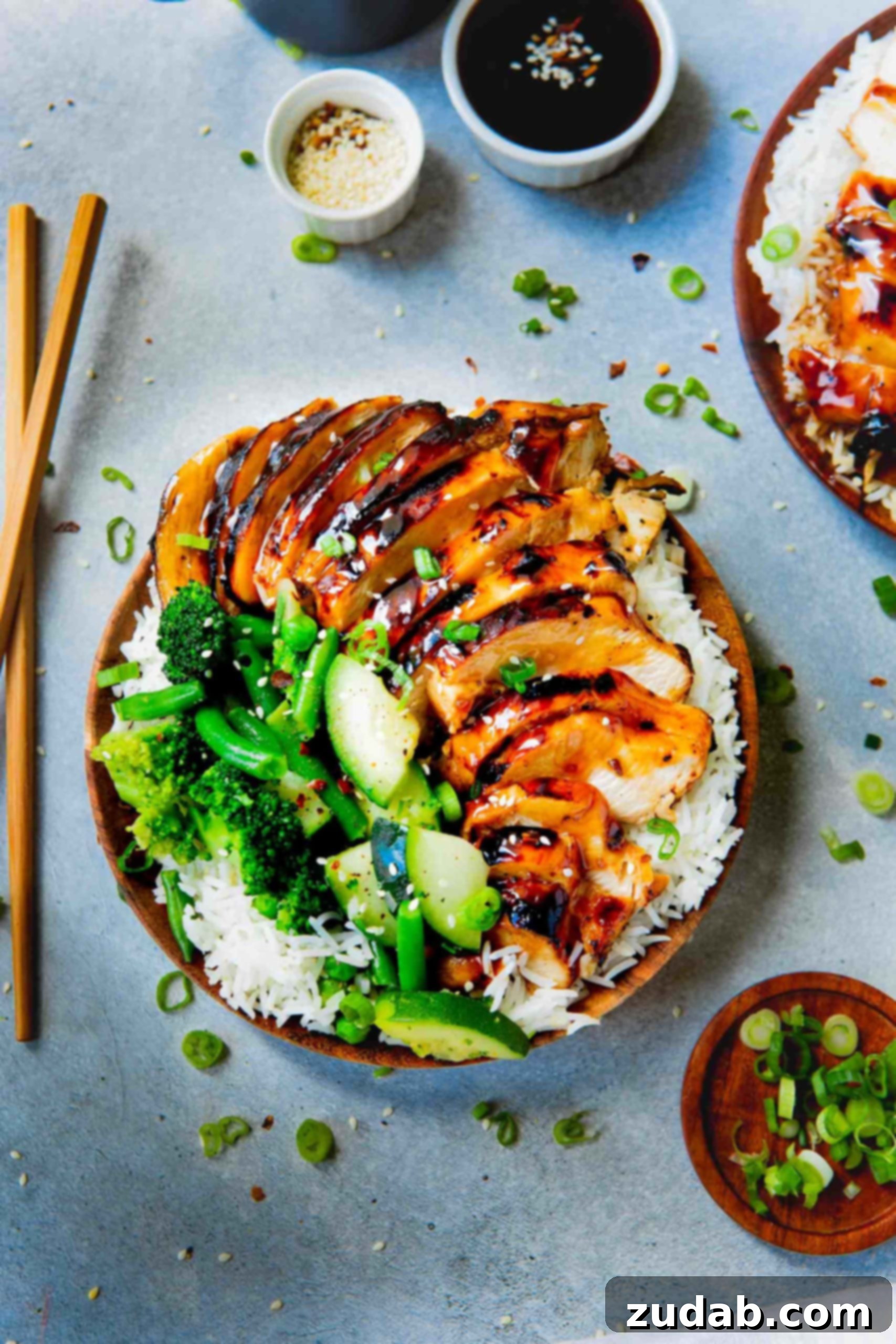 A vibrant plate featuring fluffy white rice, topped with succulent pieces of teriyaki chicken, surrounded by a colorful array of steamed broccoli, zucchini, and green beans. The dish is inviting and perfectly balanced.
