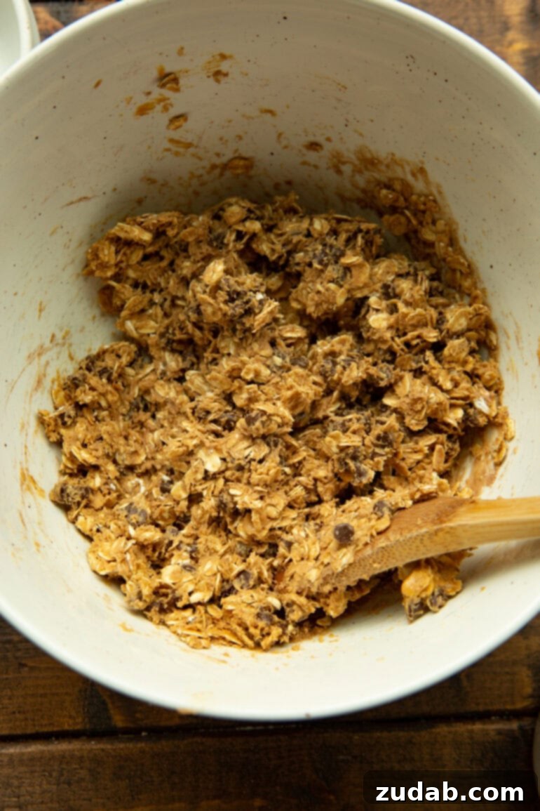 No-Bake Chocolate Protein Power Bites 5 A wooden spoon actively mixing oatmeal energy bites in a large white bowl, highlighting the ease of preparation.