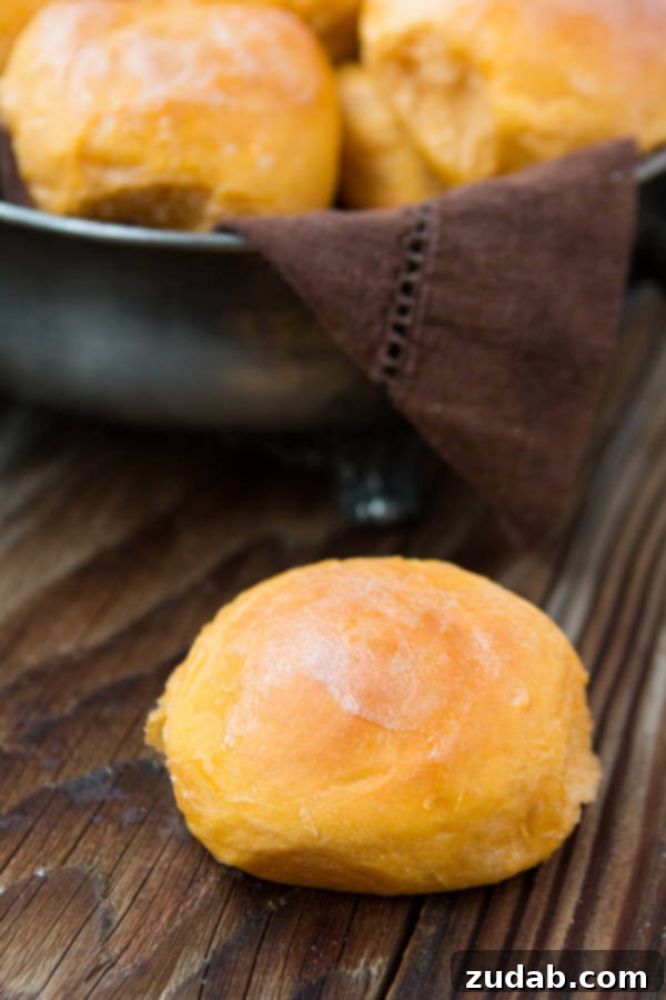 The Golden Standard: Our Irresistible Sweet Potato Rolls A single, perfectly baked sweet potato roll resting in front of a basket of more rolls, highlighting its golden crust and soft texture.