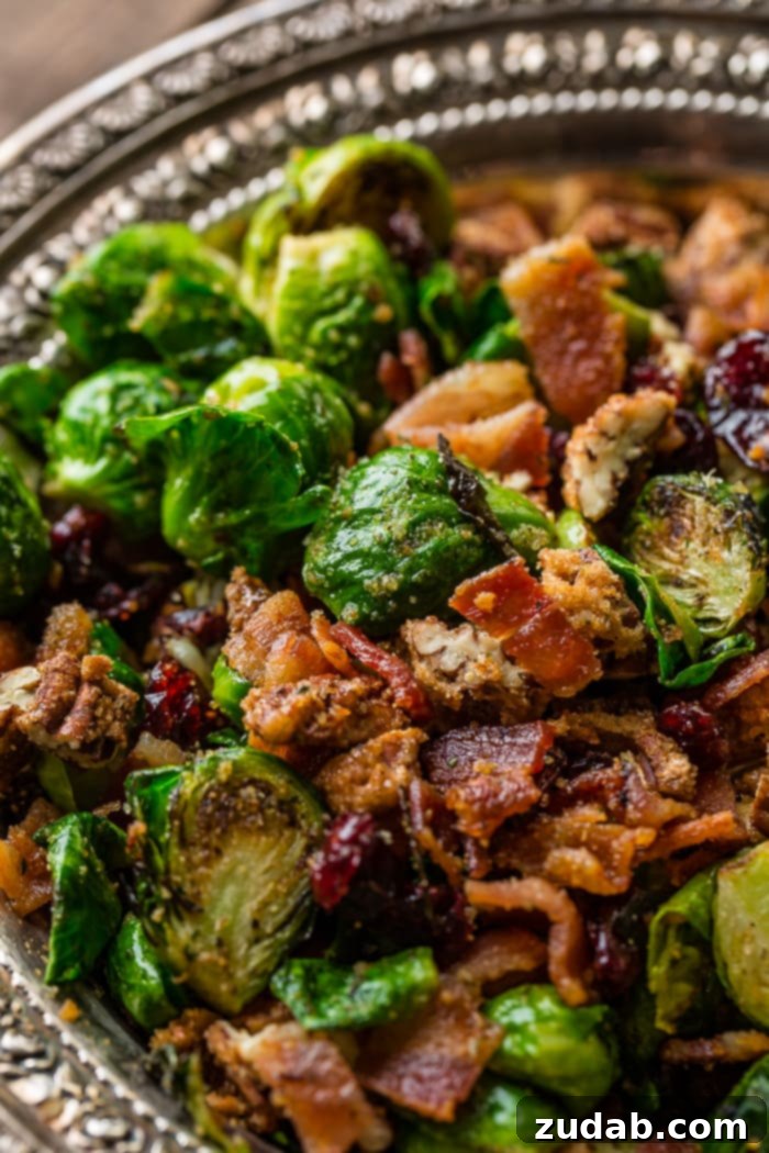 Irresistible Candied Pecan Bacon Brussels Sprouts 2 A vintage, silver bowl with flower full of bright green brussels sprouts that have been halved and pan roasted until golden brown on one side, olive oil and seasoning covering all of them and tossed with red craisins, crisp bacon and crunchy candied pecans ohsweetbasil.com