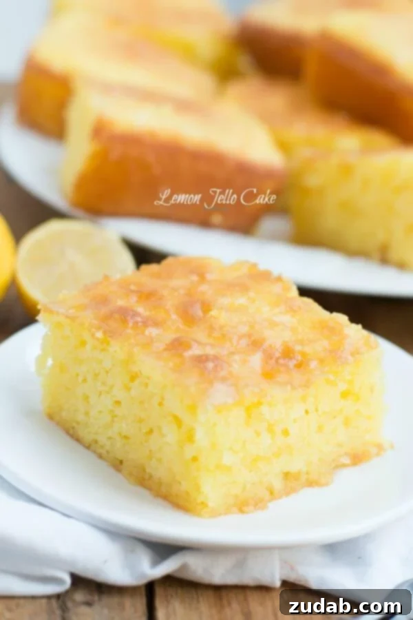 This Lemon Jello Cake is perfect for anytime of the year. The fresh tastes of summer or to brighten the winter holiday meals. A perfectly portioned slice of bright yellow Lemon Jello Cake on a simple white serving plate, highlighting its tender texture.
