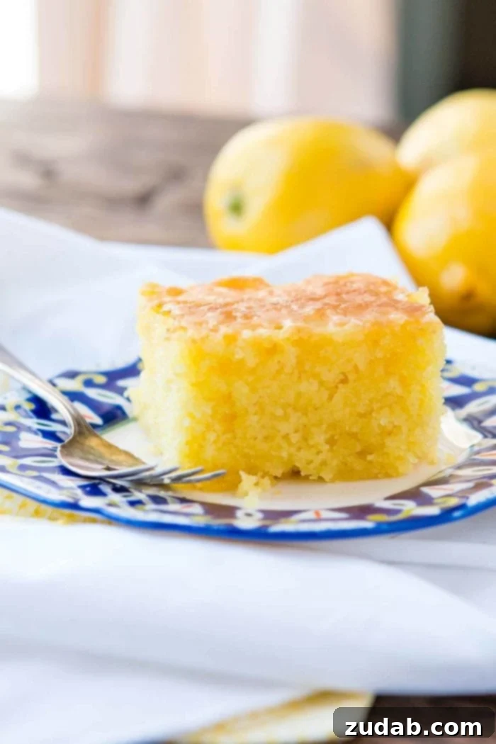 This Lemon Jello Cake is perfect for anytime of the year. The fresh tastes of summer or to brighten the winter holiday meals. A delectable slice of Lemon Jello Cake elegantly presented on a decorative plate with a gleaming silver fork beside it.