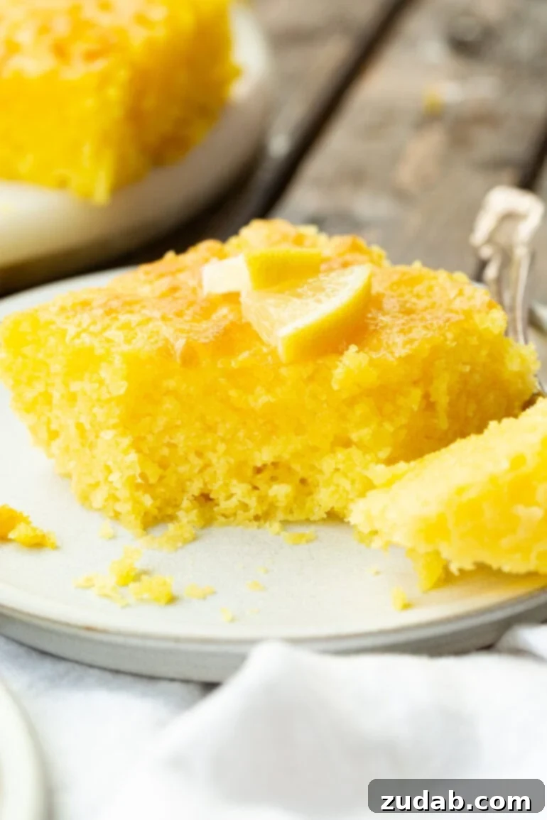 Zesty Lemon Cloud Cake 3 A close-up photo of a moist slice of Lemon Jello Cake with a bite taken, revealing its tender, yellow interior and the seeped-in lemon glaze.
