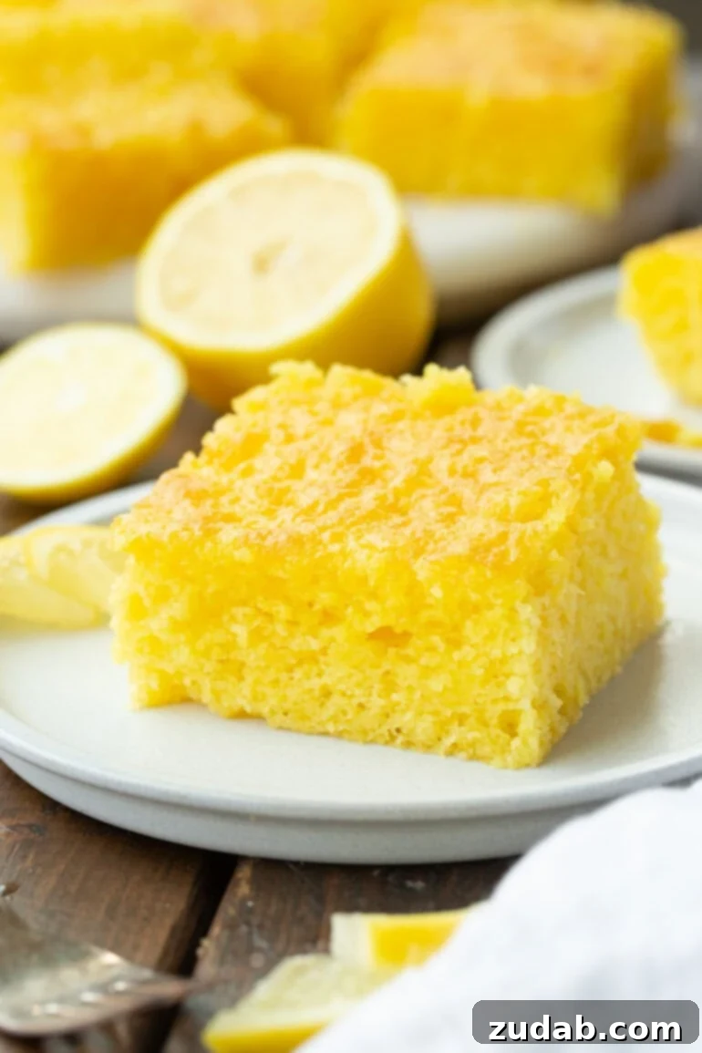 Zesty Lemon Cloud Cake 5 A glistening piece of moist lemon jello cake, perfectly glazed, resting on a small white dessert plate, ready to be enjoyed.