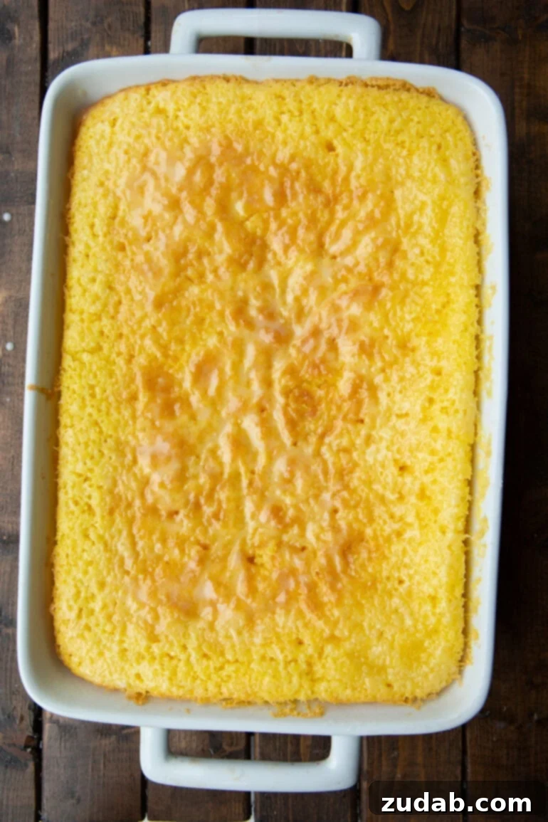 Zesty Lemon Cloud Cake 7 A beautiful, whole 9x13 inch lemon cake, perfectly baked, sitting in a white ceramic baking dish, glistening with its lemon glaze.