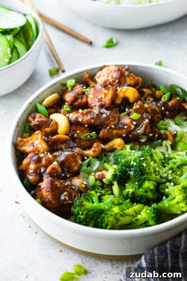 Effortless Cashew Chicken 4 A photo of a bowl of tender bites of chicken coated in a bold sauce and mixed with cashews all next to steamed broccoli florets.