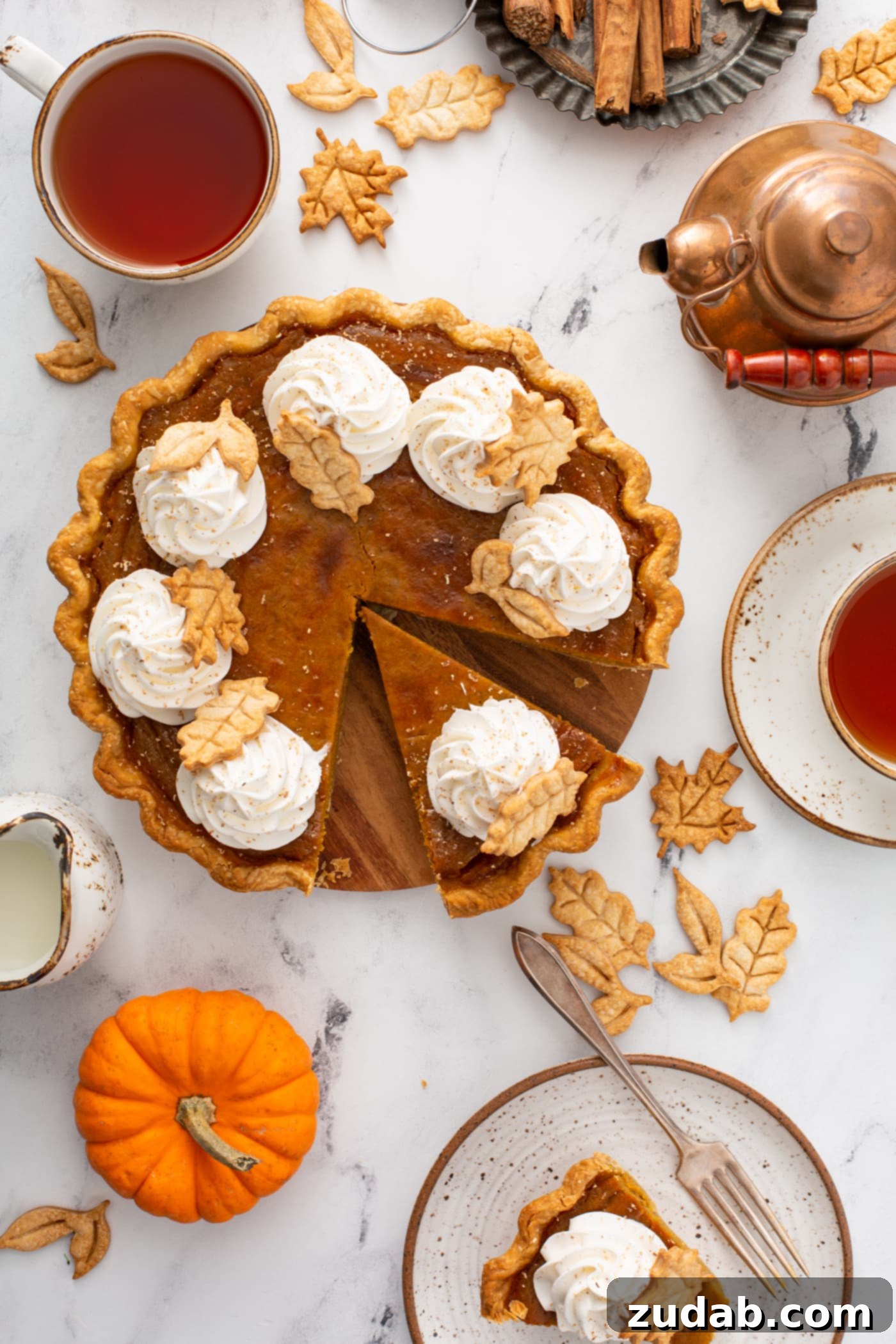 Homestyle Pumpkin Pie 2 A photo of a pumpkin pie topped with piped whipped cream and stamped pie crust leaves taken from above with a slice pulled out.