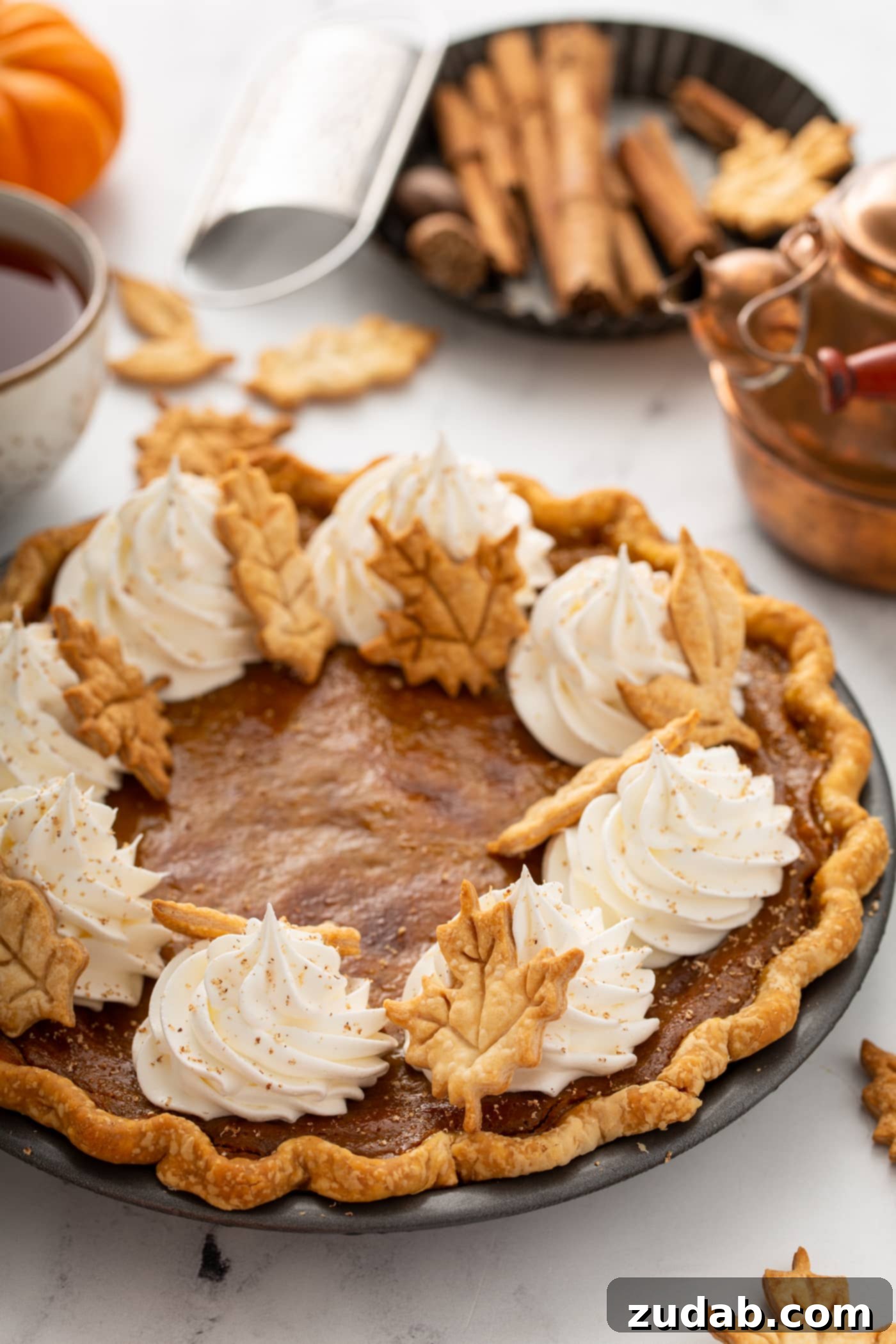 Homestyle Pumpkin Pie 4 A whole pumpkin pie topped with piped whipped cream and pie crust leaves.