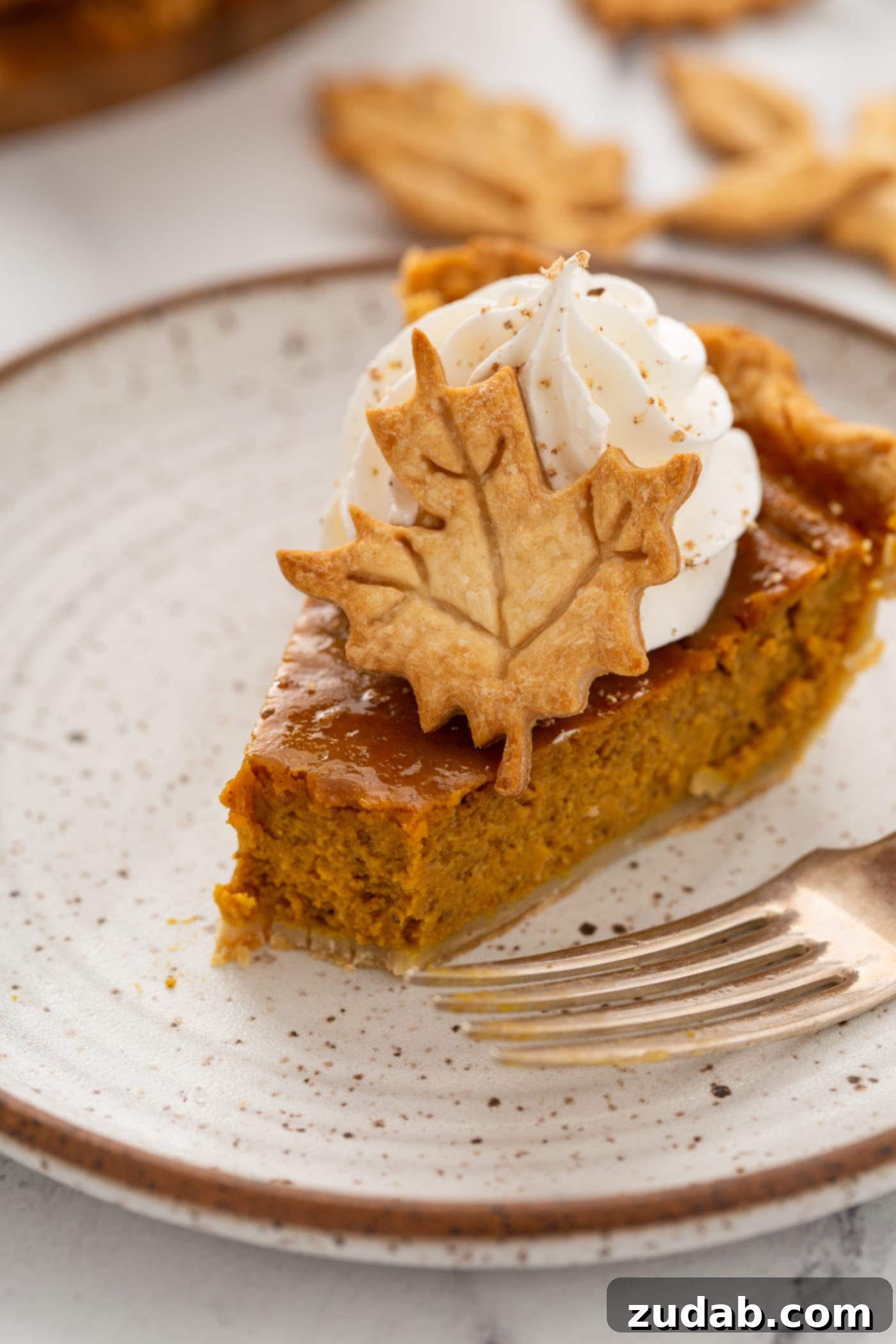 Homestyle Pumpkin Pie 9 A photo of a slice of pumpking pie with a bite removed topped with piped whipped cream and a pie crust leaf.