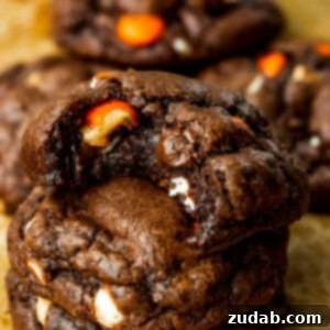 A photo of three triple chocolate Reese's cookies stacked on each other with a bite taken out of the top cookie