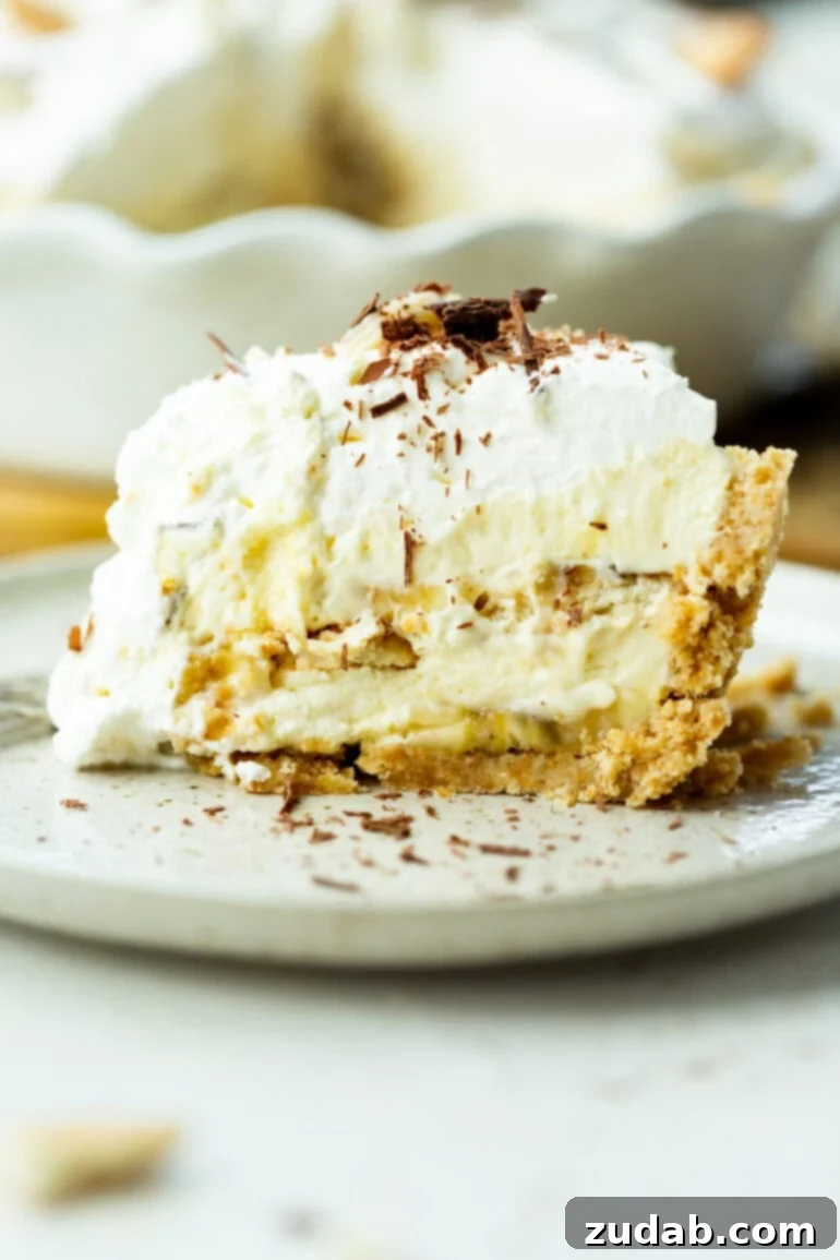 Heavenly No-Bake Banana Pudding Pie with Nilla Wafer Crust 2 A large slice of double-layered banana pudding pie, generously topped with fluffy whipped cream and delicate shaved chocolate, sitting on a white dessert plate.