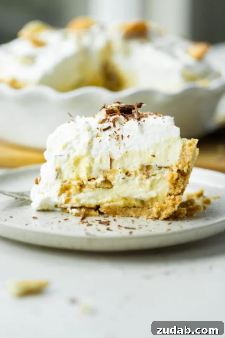 Heavenly No-Bake Banana Pudding Pie with Nilla Wafer Crust 8 A perfect cross-section view of a slice of banana pudding cream pie, neatly presented on a dessert plate, showcasing its distinct layers.