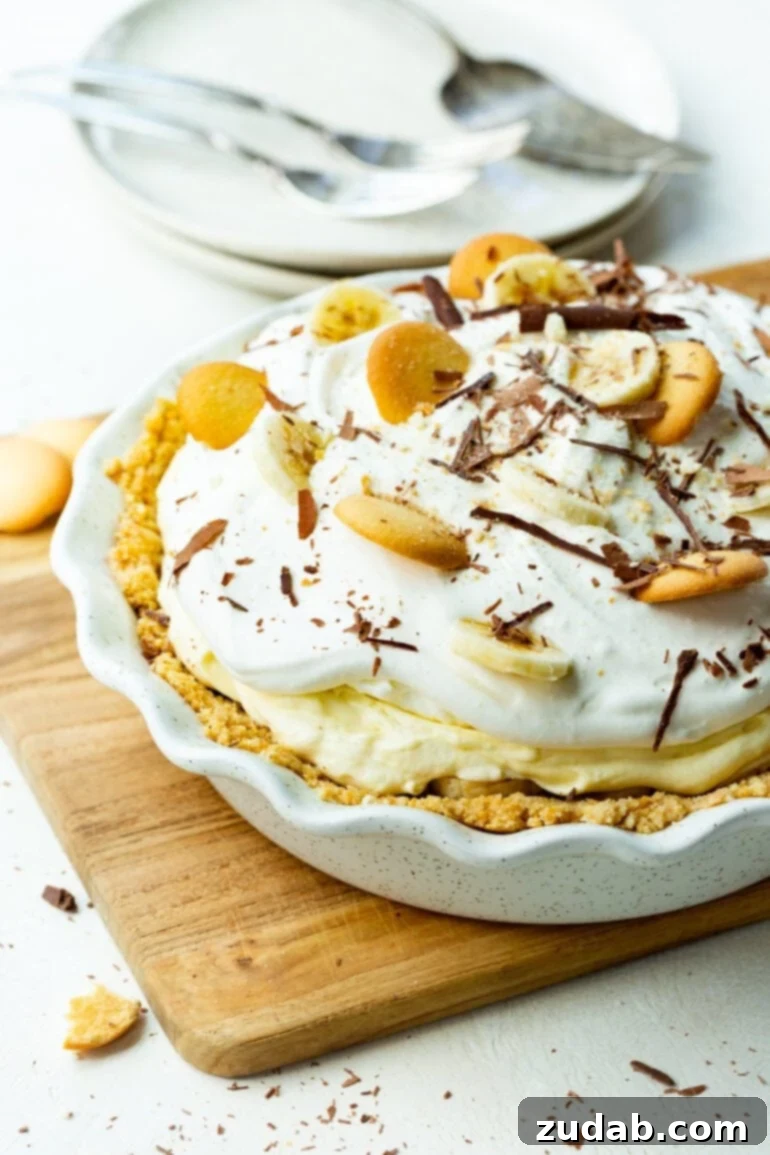 Heavenly No-Bake Banana Pudding Pie with Nilla Wafer Crust 9 A beautifully presented whole banana pudding pie in a white pie dish, topped with swirls of whipped cream, fresh banana slices, Nilla wafers, and delicate chocolate shavings.