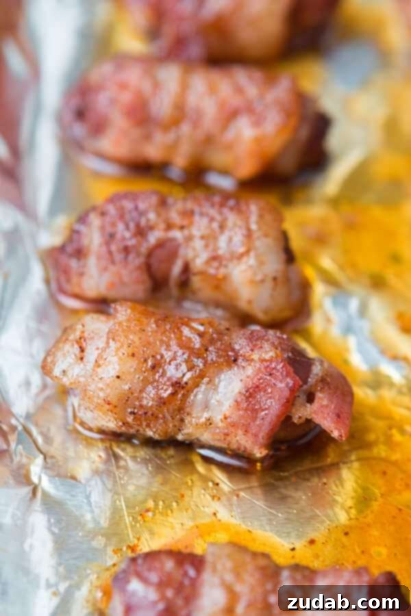 Close-up of golden-brown bacon-wrapped little smokies on a baking sheet, showcasing their caramelized coating.