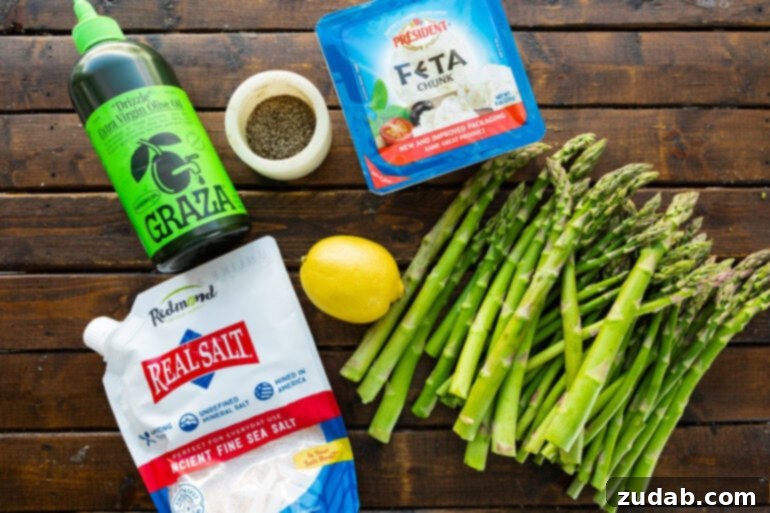 a photo taken over the top of all the ingredients for grilled lemon feta asparagus including asparagus spears, feta cheese, salt, pepper, a whole lemon and a bottle of olive oil