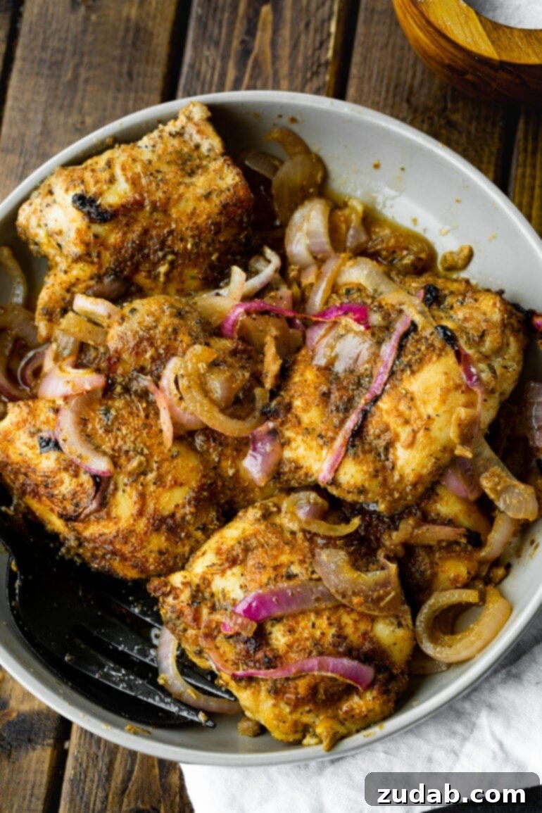 Effortless Baked Boneless Skinless Chicken Thighs 3 A photo of several golden baked chicken thighs mixed with slices of vibrant red onion, garnished with a sprinkle of fresh herbs.