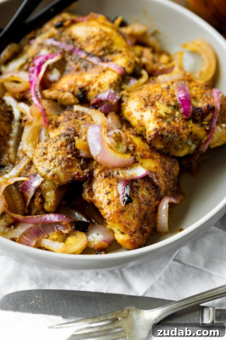 Effortless Baked Boneless Skinless Chicken Thighs 5 A large white serving bowl brimming with several golden baked chicken thighs, beautifully mixed with tender, cooked red onions, glistening with savory juices.