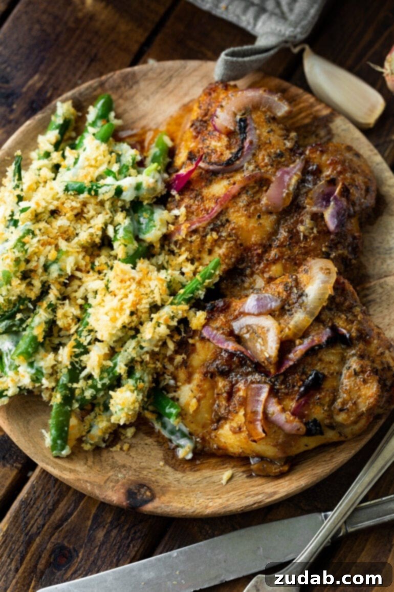 Effortless Baked Boneless Skinless Chicken Thighs 6 A wooden plate featuring two golden baked chicken thighs, beautifully seasoned, served alongside a comforting ranch green bean casserole.