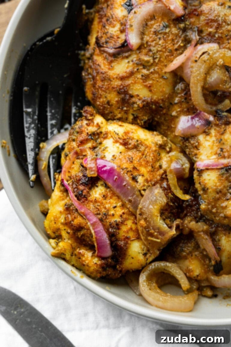 Effortless Baked Boneless Skinless Chicken Thighs 7 A close-up shot of a perfectly golden baked chicken thigh, showcasing its rich dry rub and tender, cooked red onion chunks on top.