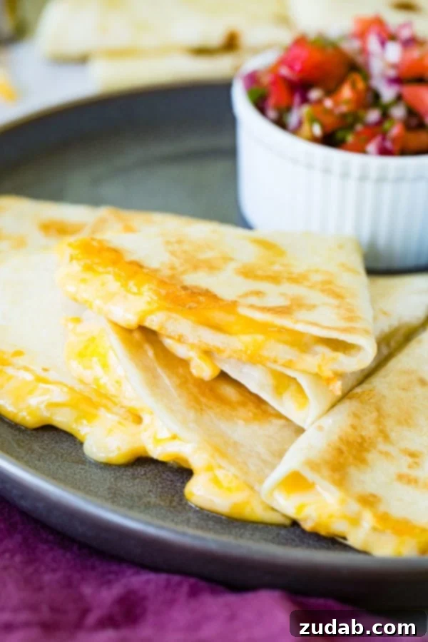 Secrets to the Best Quesadilla A photo of the best quesadilla sliced into pieces and stacked, with gooey cheese oozing out, alongside a bowl of fresh pico de gallo in the background.