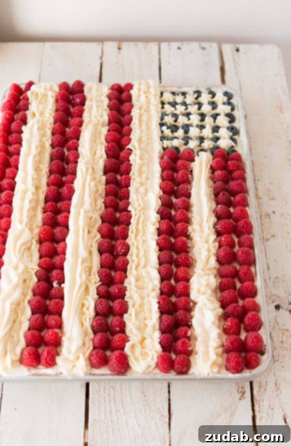 Patriotic Flag Cake Recipe: Fluffy White Cake, Creamy Frosting, and Fresh Berries for Your Celebration Close-up of a homemade Flag Cake, showing fluffy white cake, creamy whipped frosting, fresh red raspberries and blue blueberries, meticulously piped white buttercream stripes. A perfect 4th of July recipe.