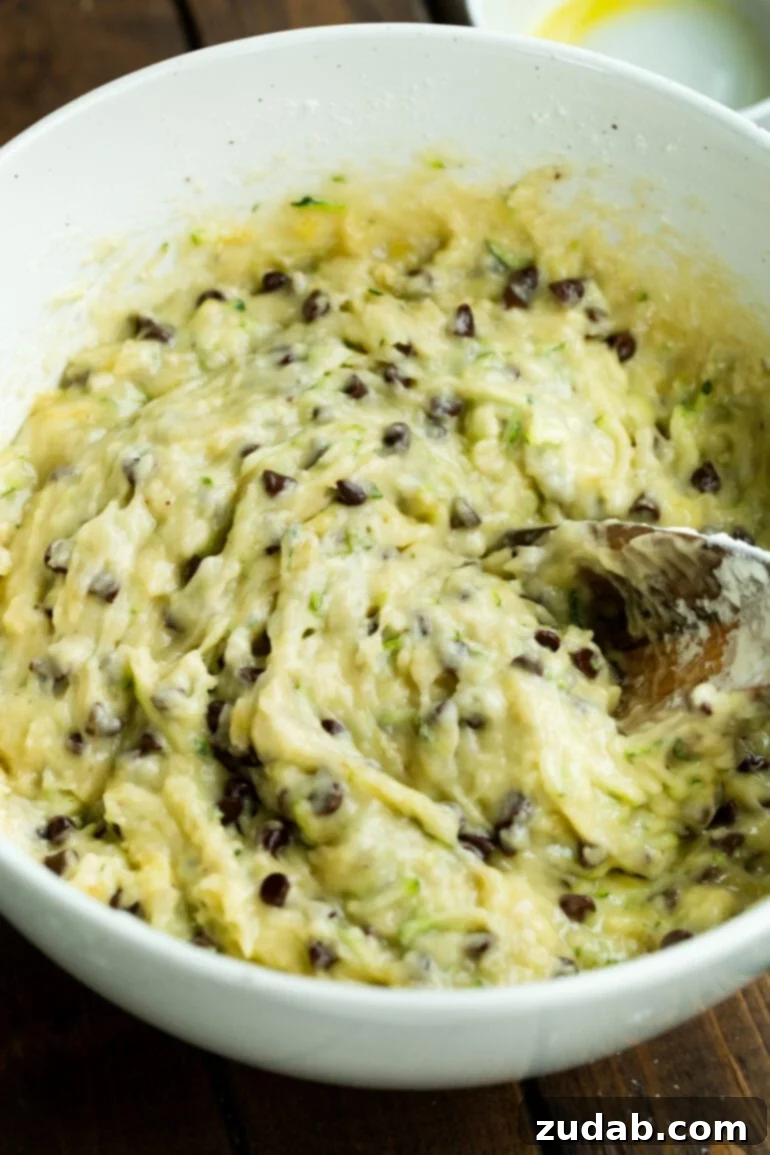 Decadent Chocolate Chip Zucchini Banana Bread 4 A photo of a wooden spoon being used to mix together the batter for chocolate chip banana zucchini bread in a large mixing bowl.
