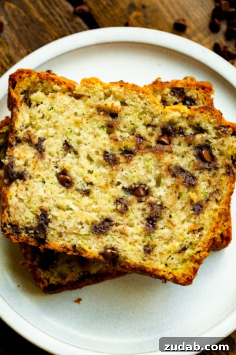 Decadent Chocolate Chip Zucchini Banana Bread 5 A photo of two slices of banana zucchini bread loaded with chocolate chips stacked on top of each other on a white dessert plate, ready to be enjoyed.