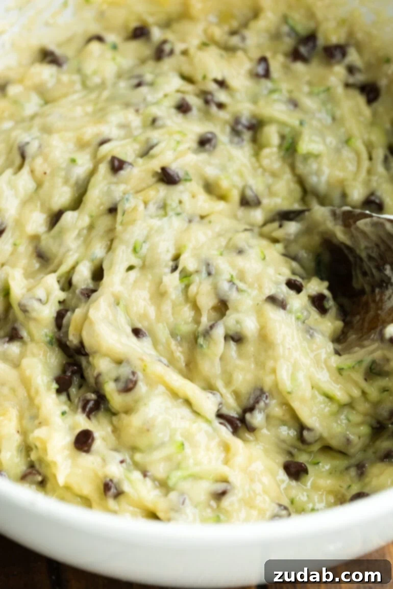 Decadent Chocolate Chip Zucchini Banana Bread 6 A photo of the batter for chocolate chip zucchini banana bread being stirred with a wooden spoon in a glass bowl.