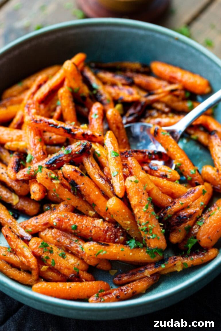 Golden Honey Garlic Roasted Carrots 4 A large silver serving spoon carefully scooping out a generous portion of golden roasted honey glazed carrots, showcasing their appealing texture and color.